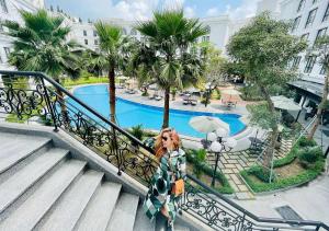 顺化Silk Path Grand Hue Hotel的站在楼梯上的女人,在游泳池旁边拿着一把伞