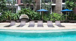 乔木提恩海滩Centara Life Maris Resort Jomtien的一组椅子和遮阳伞,位于游泳池旁