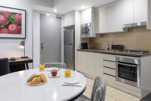 悉尼赖德北梅里顿公寓式酒店的厨房配有带面包和2杯橙汁的桌子