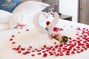 芽庄Miracle Luxury Nha Trang的两个天鹅穿着婚纱,睡在床上,床上有玫瑰花