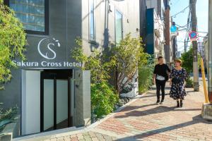 东京Sakura Cross Hotel Ueno Iriya Annex的两个女人在建筑物前的街道上走