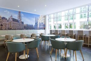 布鲁塞尔布鲁塞尔阿伦贝格大广场NH酒店的餐厅设有桌椅和大窗户。
