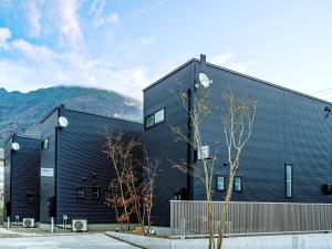 由布市Rakuten STAY HOUSE x WILL STYLE Yufuin Kawakami 103的一座黑色的建筑,背景是群山