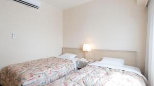 北九州Tabist Hotel Tetora Kitakyushu的一间卧室设有两张床和一张桌子上的台灯。