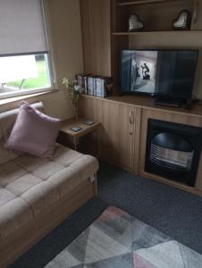 康威A22 is a 3 bedroom caravan on Whitehouse Leisure Park in Towyn near Abergele with decking and close to sandy beach的带沙发和电视的客厅