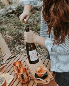 科尔斯湾Numie - Freycinet Peninsula - Glamping的野餐桌上拿着一瓶葡萄酒的女人