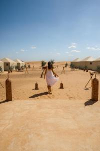 梅尔祖卡Beldi camp的穿白色衣服在沙漠中行走的女人