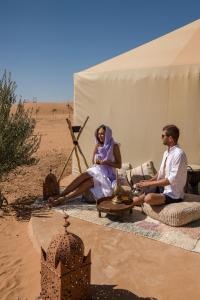 梅尔祖卡Beldi camp的坐在沙漠帐篷里的男人和女人