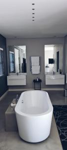 约翰内斯堡Cottage in Sandton的浴室里设有一个大型的白色浴缸,配有三面镜子