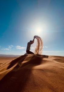 BrijaTinfou desert camp的站在沙漠中,有太阳在后面的人