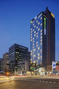 首尔ibis Styles Ambassador Seoul Myeong-dong的一座高大的建筑,旁边有一个绿色的标志