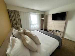 ChaurayHôtel Akena Chauray-Niort的卧室配有带枕头的白色床和电视。