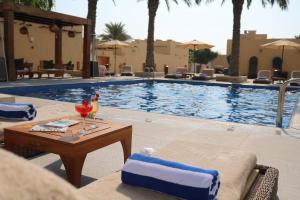 多哈Souq Al Wakra Hotel Qatar By Tivoli的一个带桌椅的游泳池,旁边是桌子