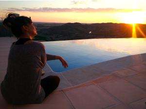 Zafra de ZáncaraCasas Rurales Planeta Chicote的坐在游泳池边欣赏日落的女人