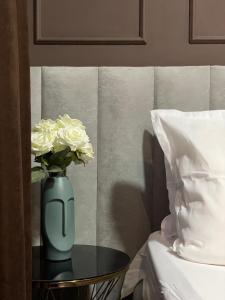 阿克托比Hotel NOMAD的一张蓝色的花瓶,上面有白色的玫瑰花,放在床边的桌子上