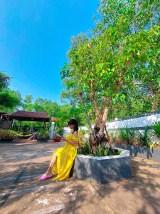 富国Ben Guesthouse Phu Quoc的站在树旁的穿着黄色衣服的女人