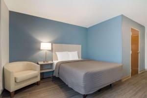 莫里斯维尔WoodSpring Suites Morrisville - Raleigh Durham Airport的蓝色卧室,配有床和椅子