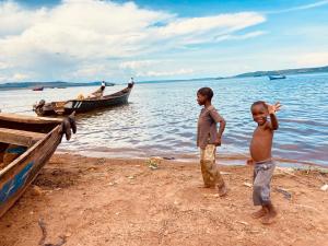 金贾Home On The Nile water front Cottage的两个男孩站在海滩上,靠近一艘船