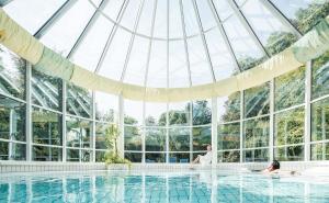巴特哈尔EurothermenResort Bad Hall - Hotel Miraverde的坐在游泳池的玻璃房子里的男人和女人