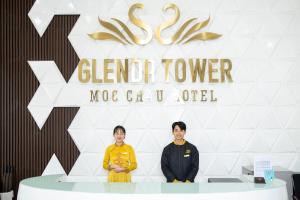木州县Glenda Tower Moc Chau Hotel的两个妇女站在桌子前,有标志