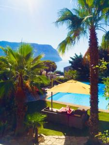 卡西斯Astoria Villa maison d hôtes Appartement vue mer avec piscine的棕榈树游泳池,以及躺在沙发和遮阳伞上的人员