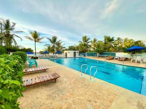 科韦尼亚斯Condominio bahia blanca的一个带长椅和遮阳伞及棕榈树的游泳池