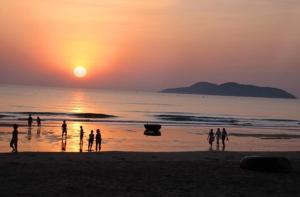 格卢市社Khách Sạn Tuấn Thảo Cửa Lò的一群人,在日落时站在海滩上