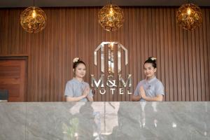 万荣M&M Hotel的两个女孩站在一个大理石柜台后面,站在一个房间里