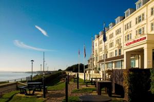 伯恩茅斯万豪伯恩茅斯高崖酒店的毗邻大海的带桌子和长凳的酒店