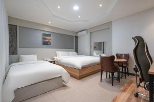 IksanBYTHS CURVE HOTEL JEONGBUK IKUSAN的酒店客房带两张床和一张桌子以及椅子。