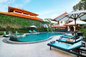 勒吉安Royal Tunjung Hotel & Villa Legian - CHSE Certified的一座带椅子和遮阳伞的游泳池位于一座建筑旁边