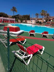 马斯帕洛马斯Casa samu camping PasitoBlanco的游泳池旁设有红色和白色的椅子