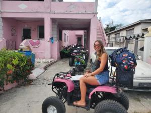 拿骚达粉白宫旅舍的坐在粉色房子前的轮子上的女人