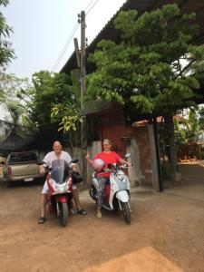 南邦Baan Mali Lampang Homestay的停放在房子前面的摩托车上的两个人