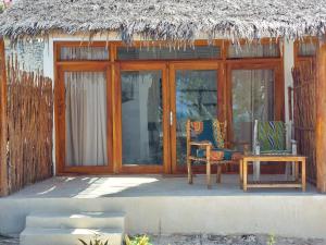 帕杰Jaribu Beach Hotel的房屋设有两把椅子和一张桌子,屋顶茅草屋顶