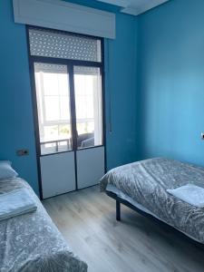 VilladesusoAlojamiento Camino Portugues Oia的蓝色的客房设有两张床和滑动玻璃门。