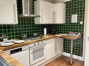 布伦特伍德Brackens的厨房设有绿色瓷砖墙壁和白色橱柜。