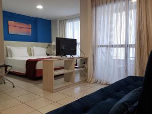 纳塔尔Janastí Suítes Praia de Ponta Negra的一间卧室配有一张床、一台电视和一张沙发