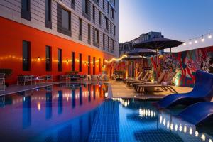 迪拜Aloft Dubai South的一座带椅子和遮阳伞的游泳池位于一座建筑旁边