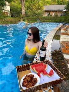 巴位Queen's Homestay Ba Vì - Venuestay的游泳池里的女人,喝一瓶葡萄酒和西瓜