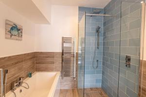 伊尔弗勒科姆Ultimate Harbourside的浴室设有浴缸和蓝色瓷砖淋浴。