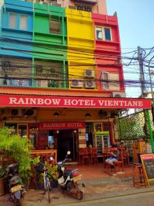 万象Rainbow Hotel Vientiane的一座五彩缤纷的建筑,前面坐着一个男人