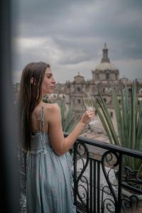 墨西哥城Zocalo Central & Rooftop Mexico City的站在阳台上的女人,拿着一杯葡萄酒