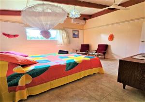 拉罗汤加Ann's Beach House的一间卧室配有一张色彩缤纷的床、两把椅子和一扇窗户
