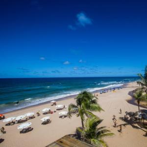 萨尔瓦多Pousada Mares de Stella的海滩上拥有遮阳伞和棕榈树,还有大海