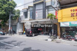 日惹Crown Residence near Tugu Yogyakarta Mitra RedDoorz的一条城市街道上的红伙伴商店,摩托车停在前面