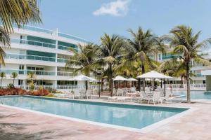 帕纳米林Qavi - Flat em Resort Beira Mar Cotovelo #InMare57的大楼前的游泳池配有椅子和遮阳伞