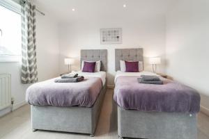 伦敦Dwellers Delight Living Ltd Serviced Accommodation, Chigwell, London 3 bedroom House, Upto 7 Guests, Free Wifi & Parking的卧室内的两张床,配有紫色毯子和枕头