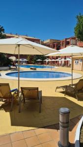 蓬塔翁布里亚Apartment Punta Umbría Luxury的一个带两把遮阳伞和两把椅子的游泳池