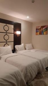 麦加فندق البيرق的一间卧室配有三张床、白色床单和绘画
